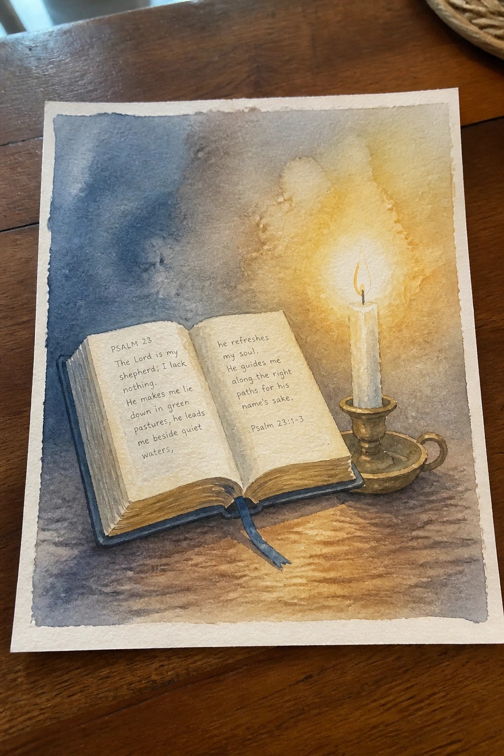 Watercolor of open Psalm 23 book beside glowing candle in holder on wood.