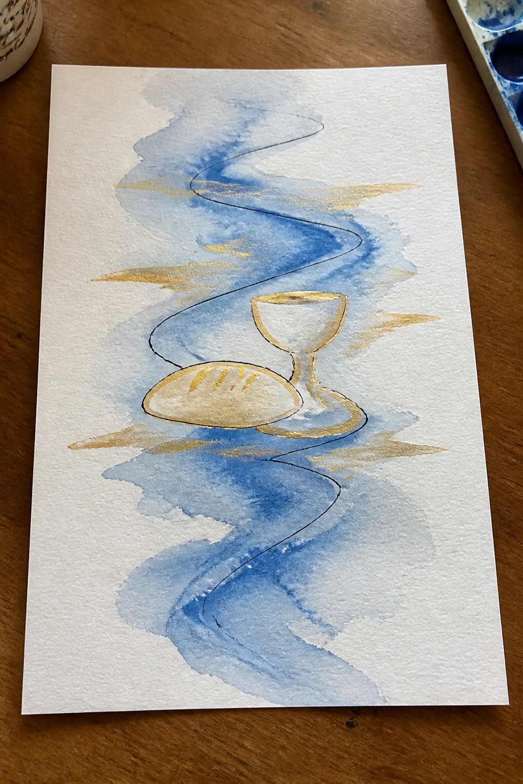 Watercolor of bread loaf and chalice amid flowing blue washes with gold accents