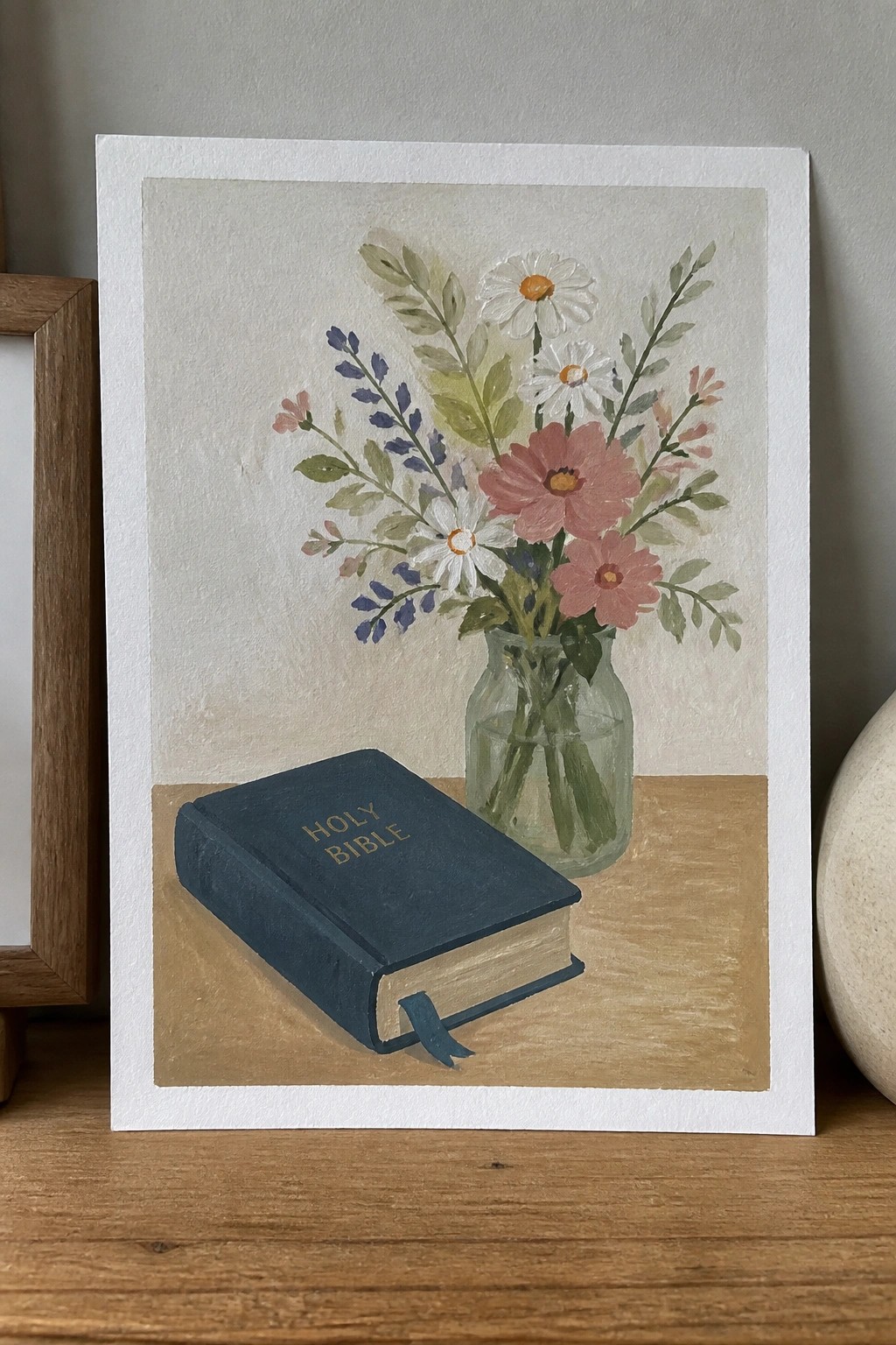 Watercolor of blue Holy Bible beside glass vase of pink and white flowers on wood.