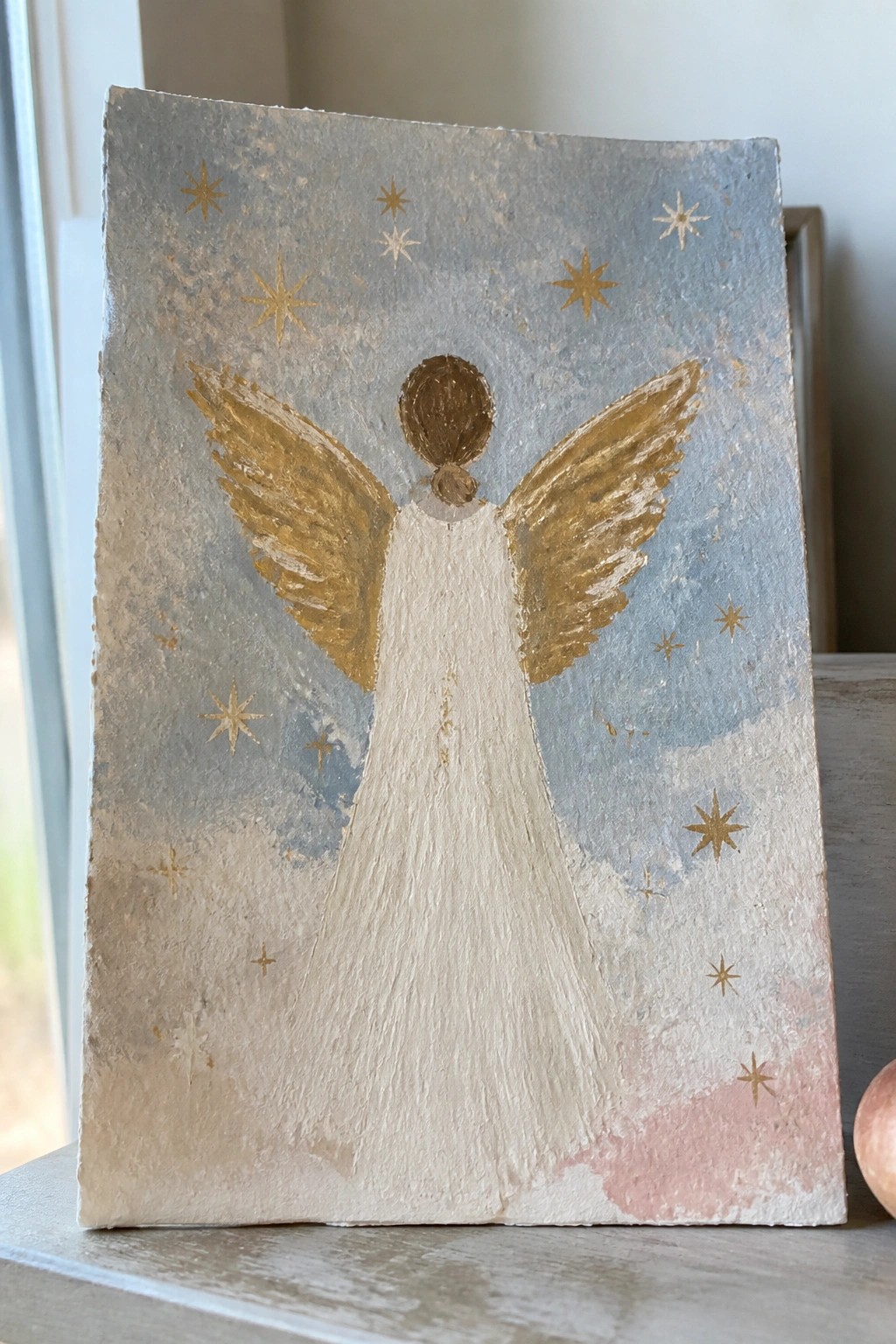 Hand-painted angel with golden wings, white gown, brown bun, and scattered stars