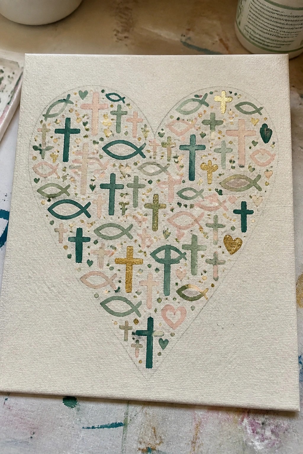 Heart-shaped canvas with colorful crosses, fish symbols, and hearts in green, pink, and gold.