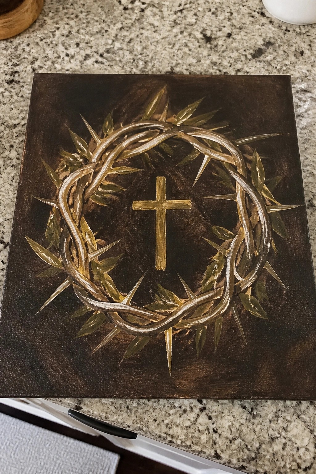 Gold crown of thorns encircling a cross on dark brown canvas.