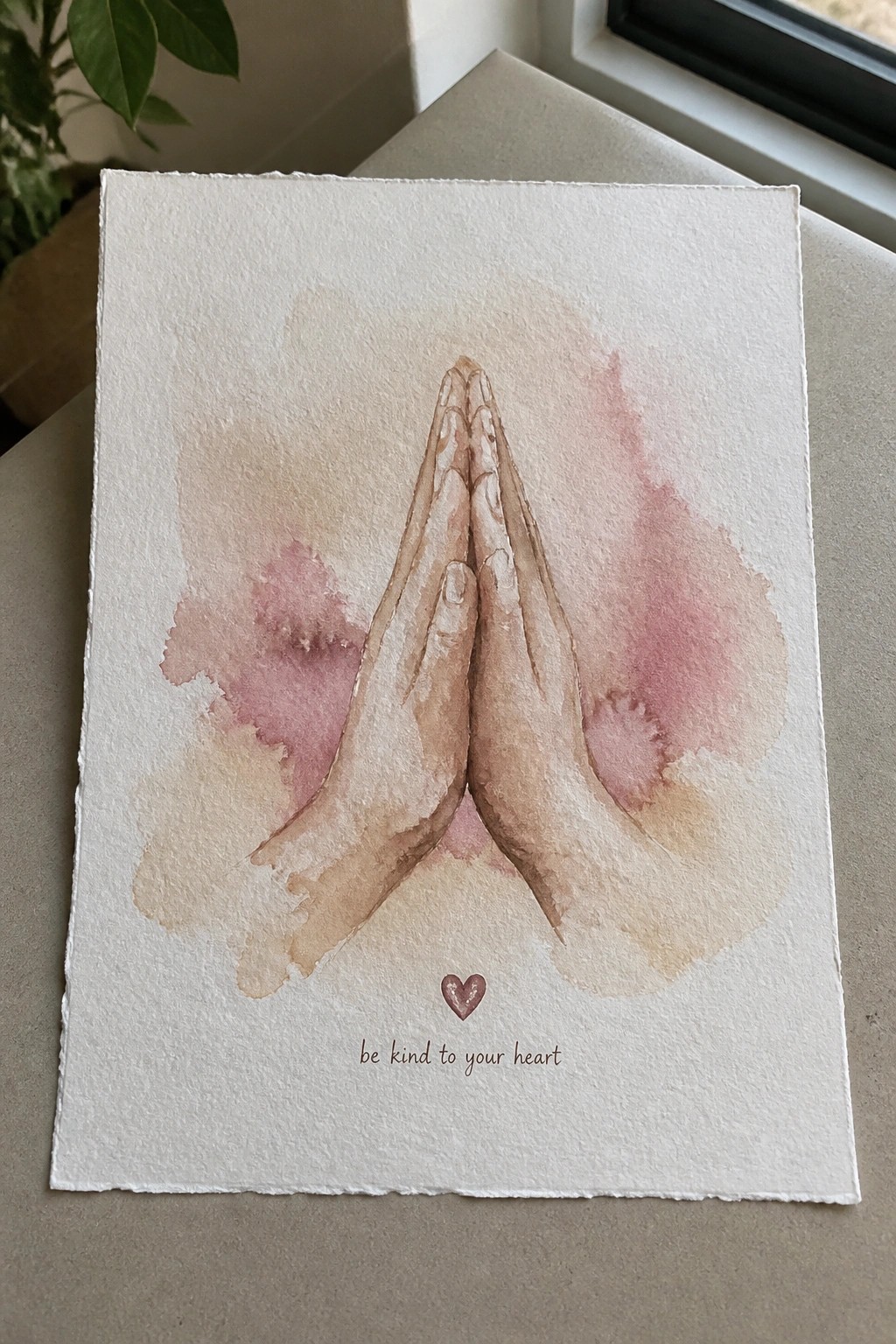 Watercolor of praying hands in soft pink and beige washes with heart and text below