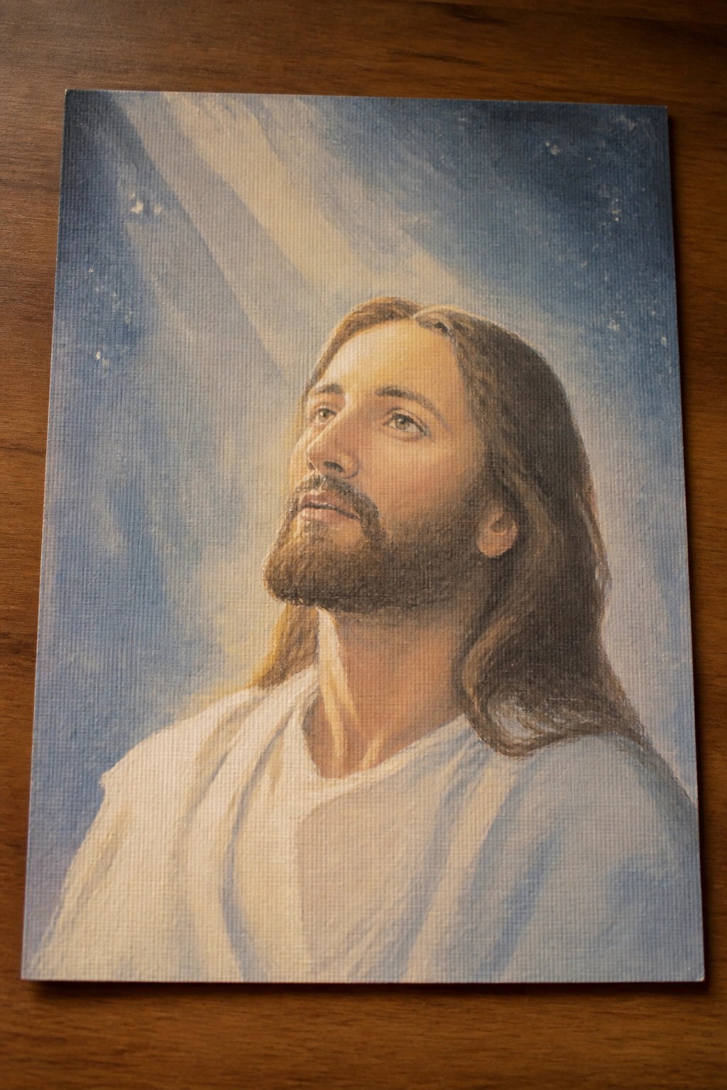 Bearded Jesus in white robe gazing upward at light rays in starry blue sky painting