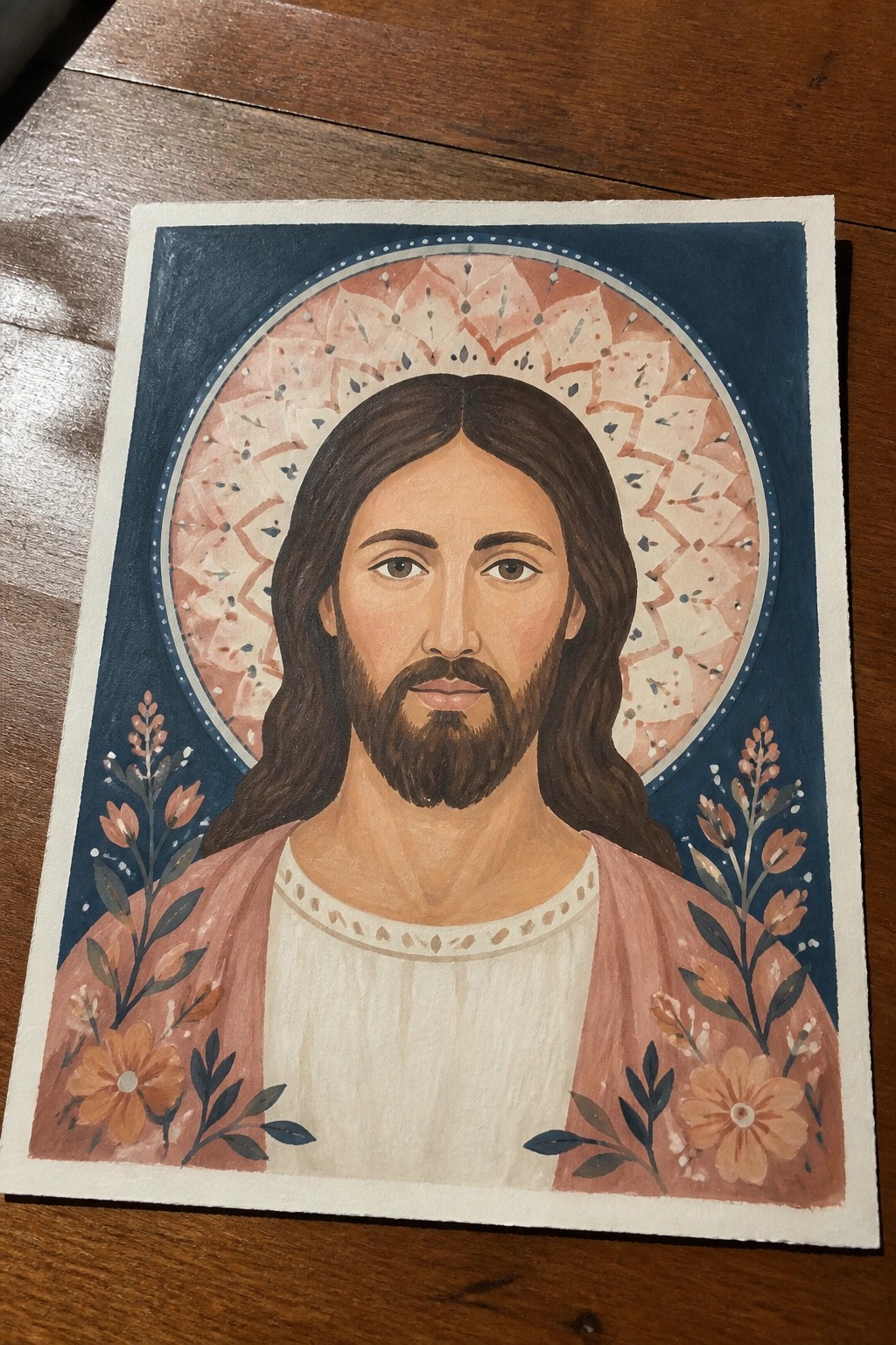 Watercolor portrait of Jesus with long brown hair and beard, pink robe, large patterned halo, and orange flowers on both sides against a dark blue background.