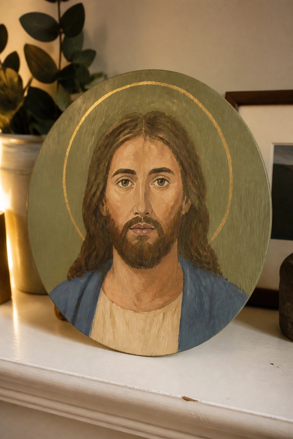 Round painted portrait of Jesus with long hair, beard, blue robe and gold halo on green.