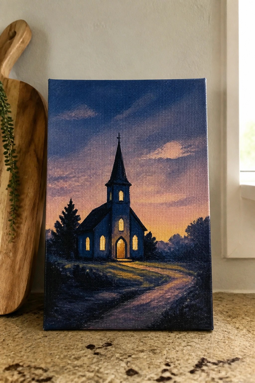 Canvas painting of blue church with glowing windows at sunset beside wooden board