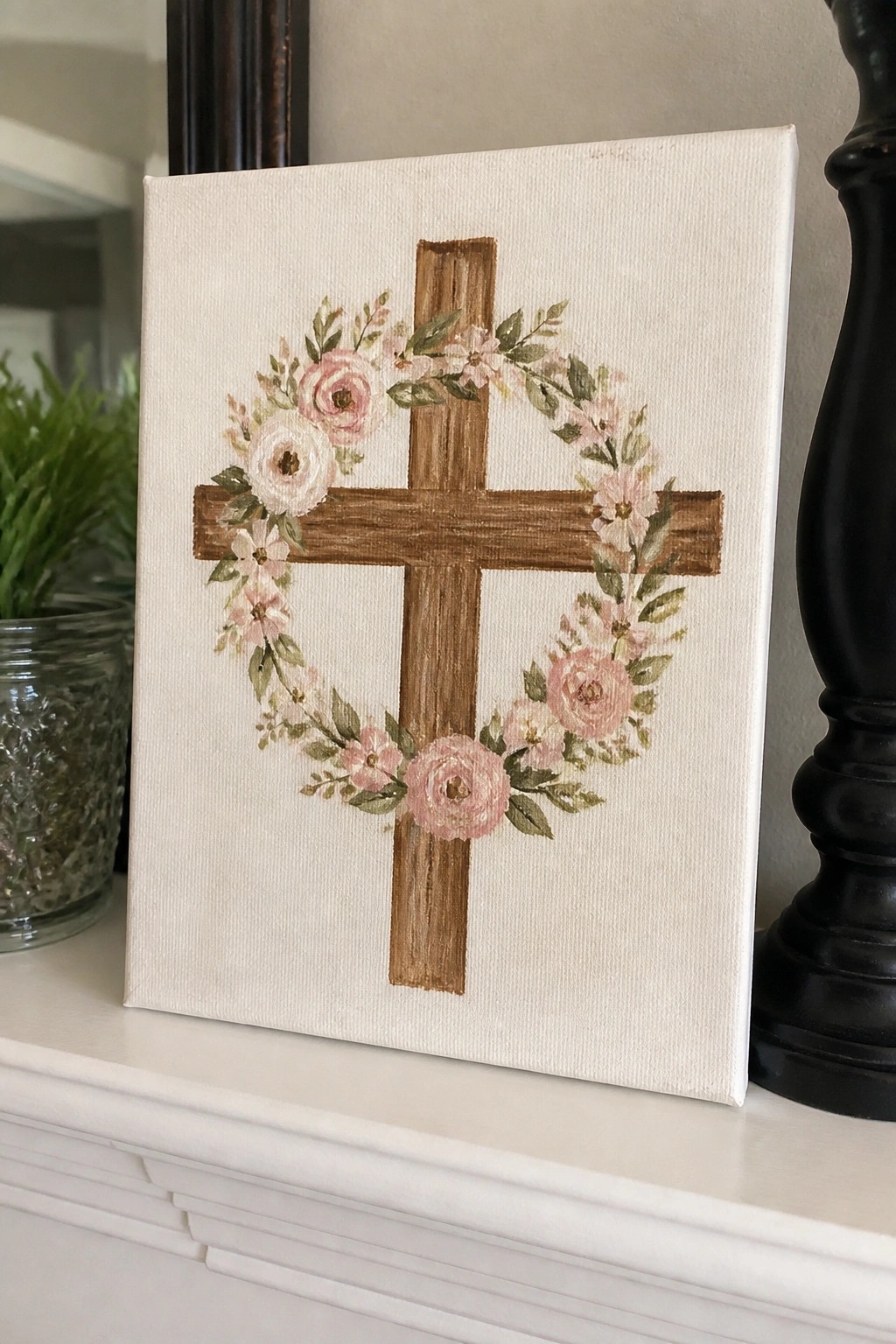 Canvas with brown cross and pink floral wreath on white mantelpiece