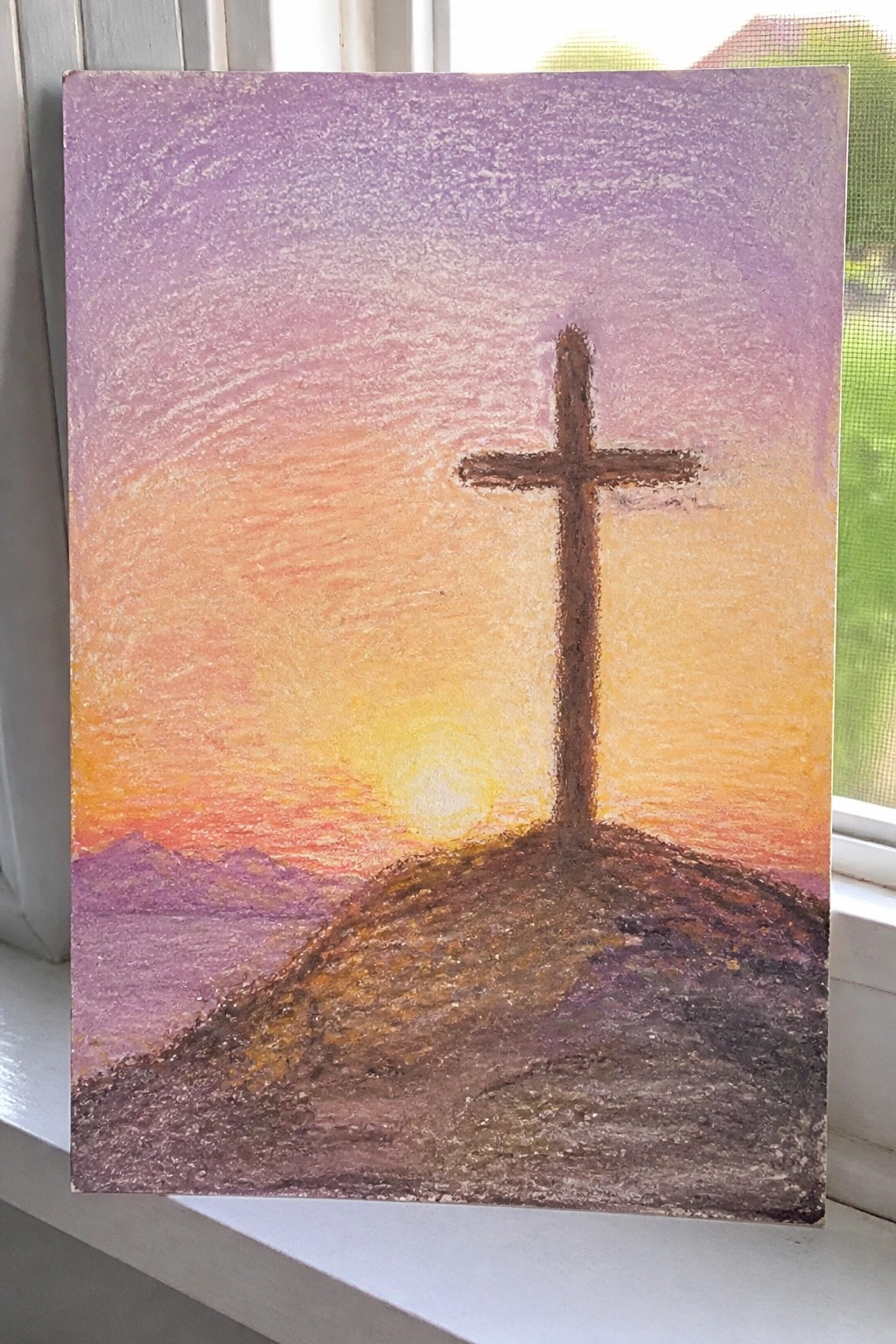 Brown cross atop a hill against a vibrant orange-purple sunset sky