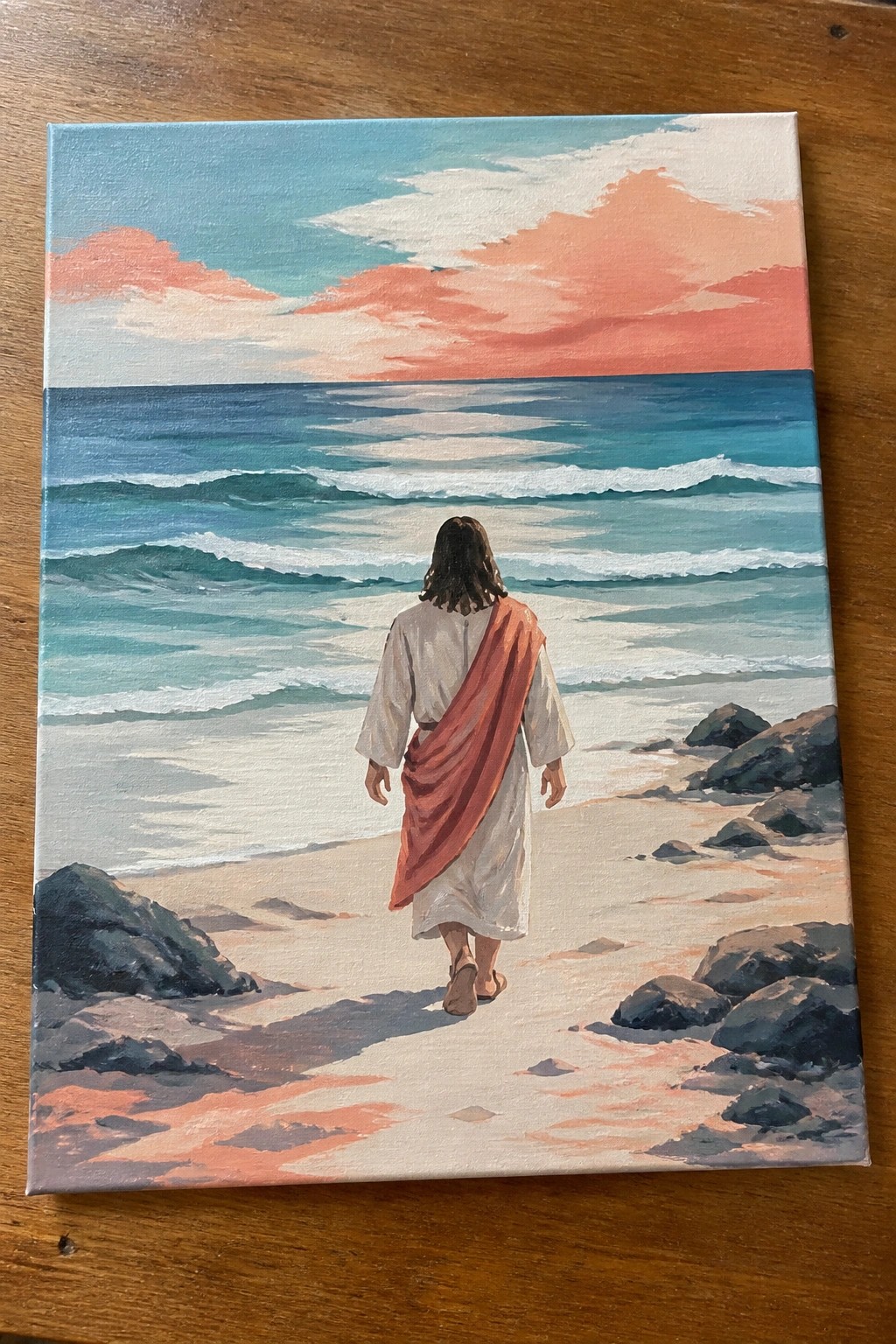 Figure in white robe with red sash walking barefoot toward ocean at sunset