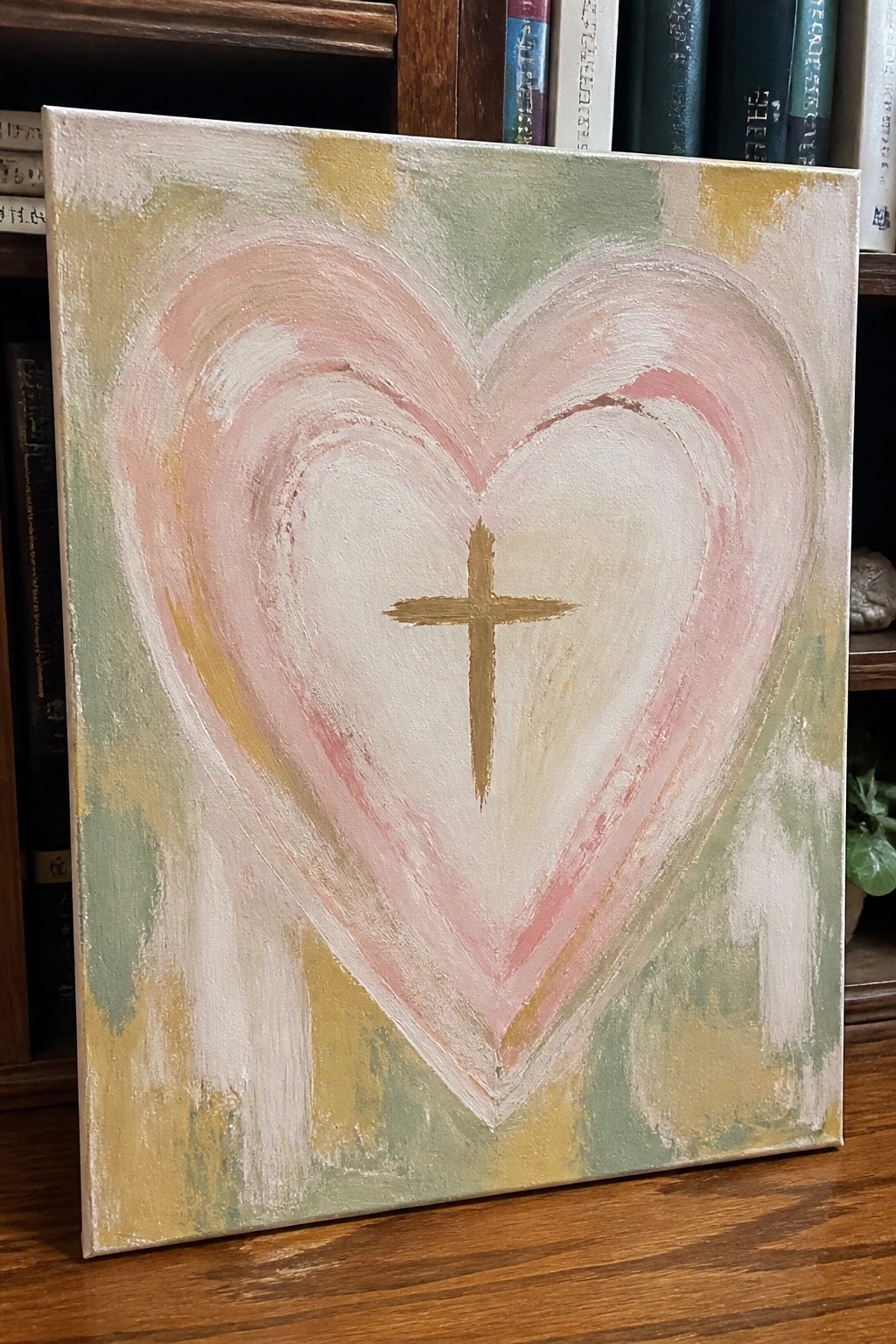 Abstract canvas painting of pink-white heart with gold cross on pastel background