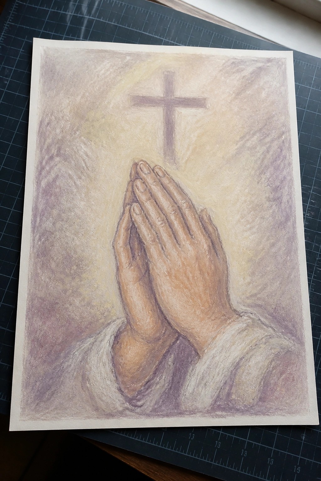 Clasped praying hands in white sleeves below a glowing cross in soft pastels