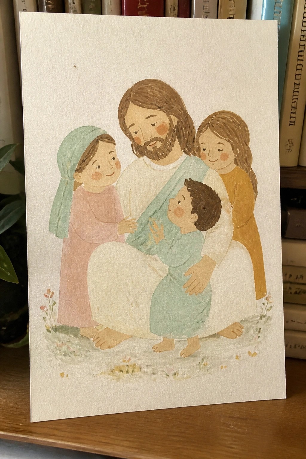 Watercolor of Jesus in white and teal robe embracing three barefoot children on flowery grass