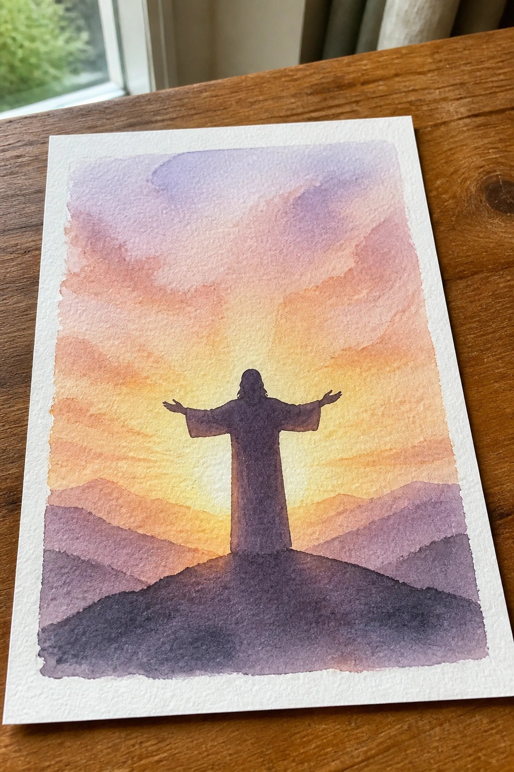 Watercolor of robed silhouette with arms outstretched on hill under vibrant sunset sky.