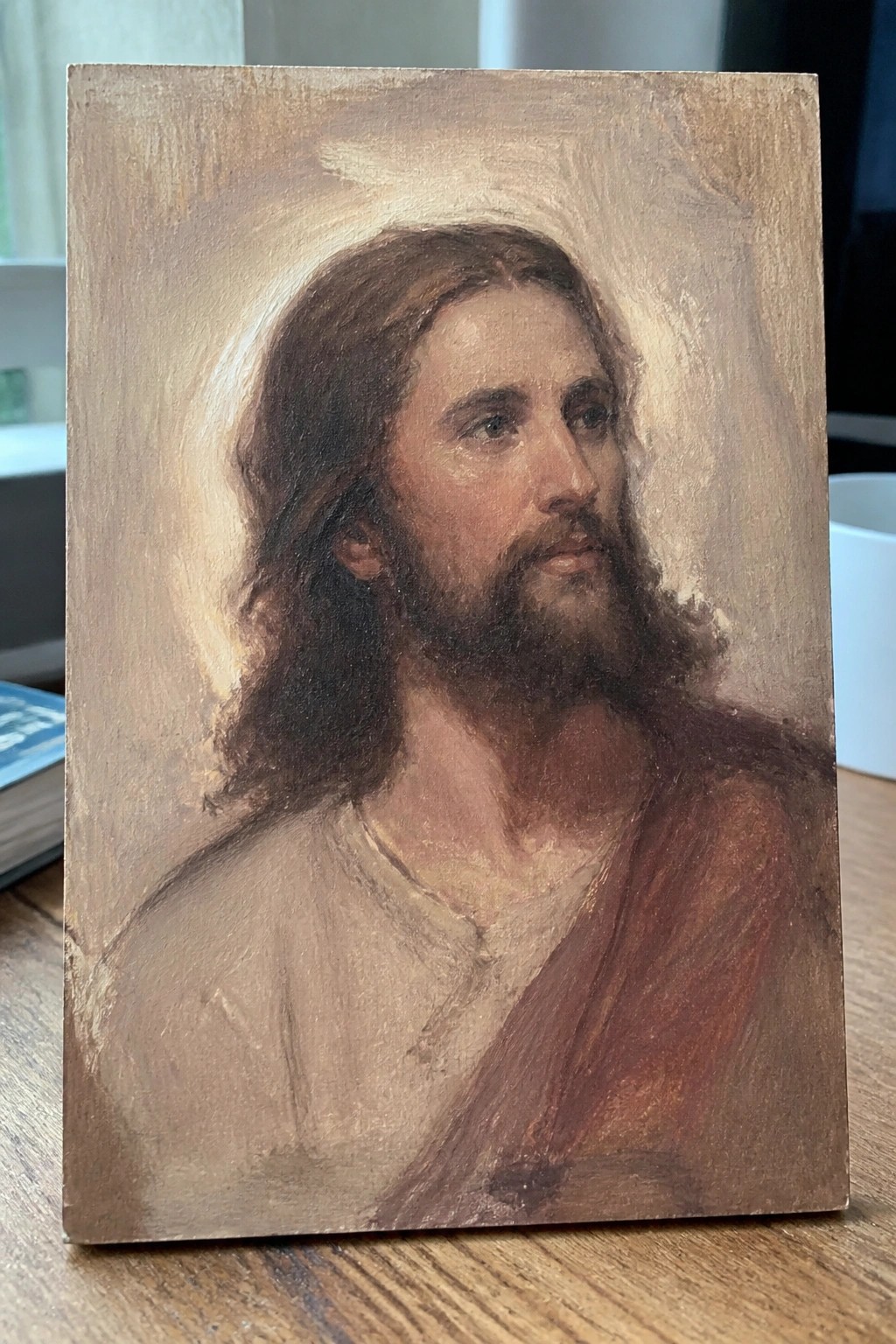 Classical painting of Jesus with long brown hair, beard, halo in white tunic and red robe.