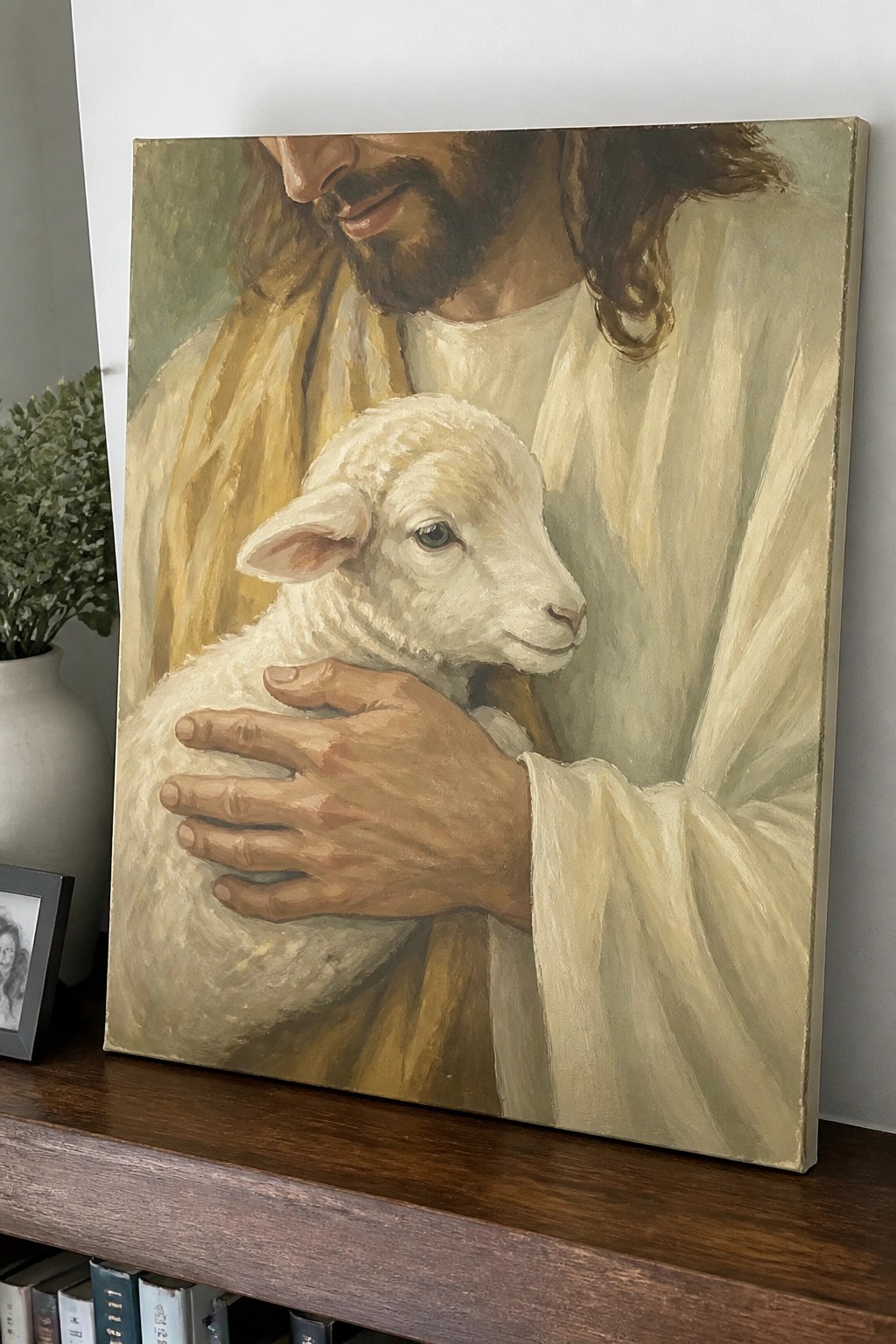 Jesus in white and gold robes cradling white lamb, painting on wooden shelf.