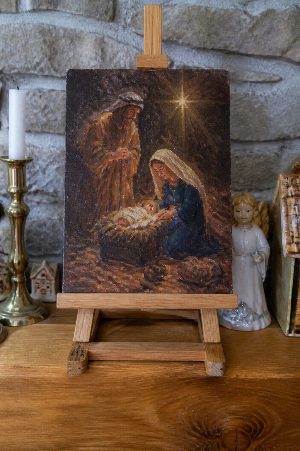 Nativity oil painting on easel with Mary in blue, Joseph, manger, star, lit candle, and angel.