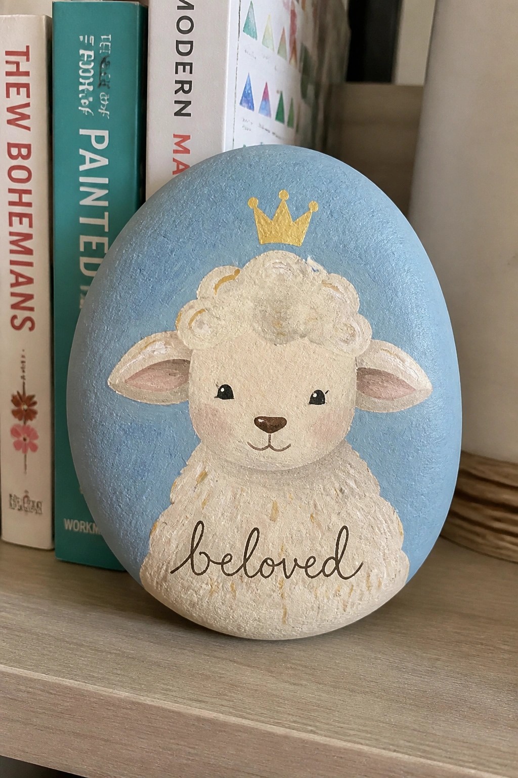 Light blue painted rock with crowned lamb and 
