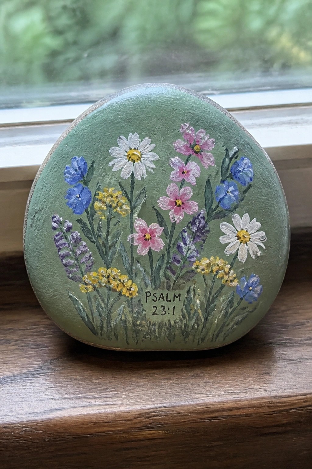 Green painted rock with colorful wildflowers and Psalm 23:1 on wooden sill