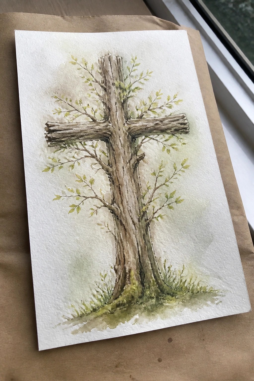Watercolor of wooden cross with green leaves sprouting from rough bark branches.