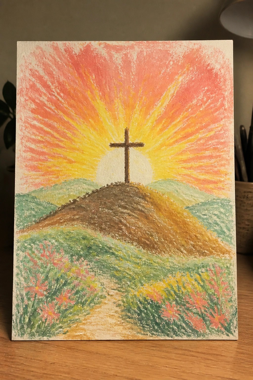 Cross on hill under vibrant orange-yellow sun rays with pink wildflowers below