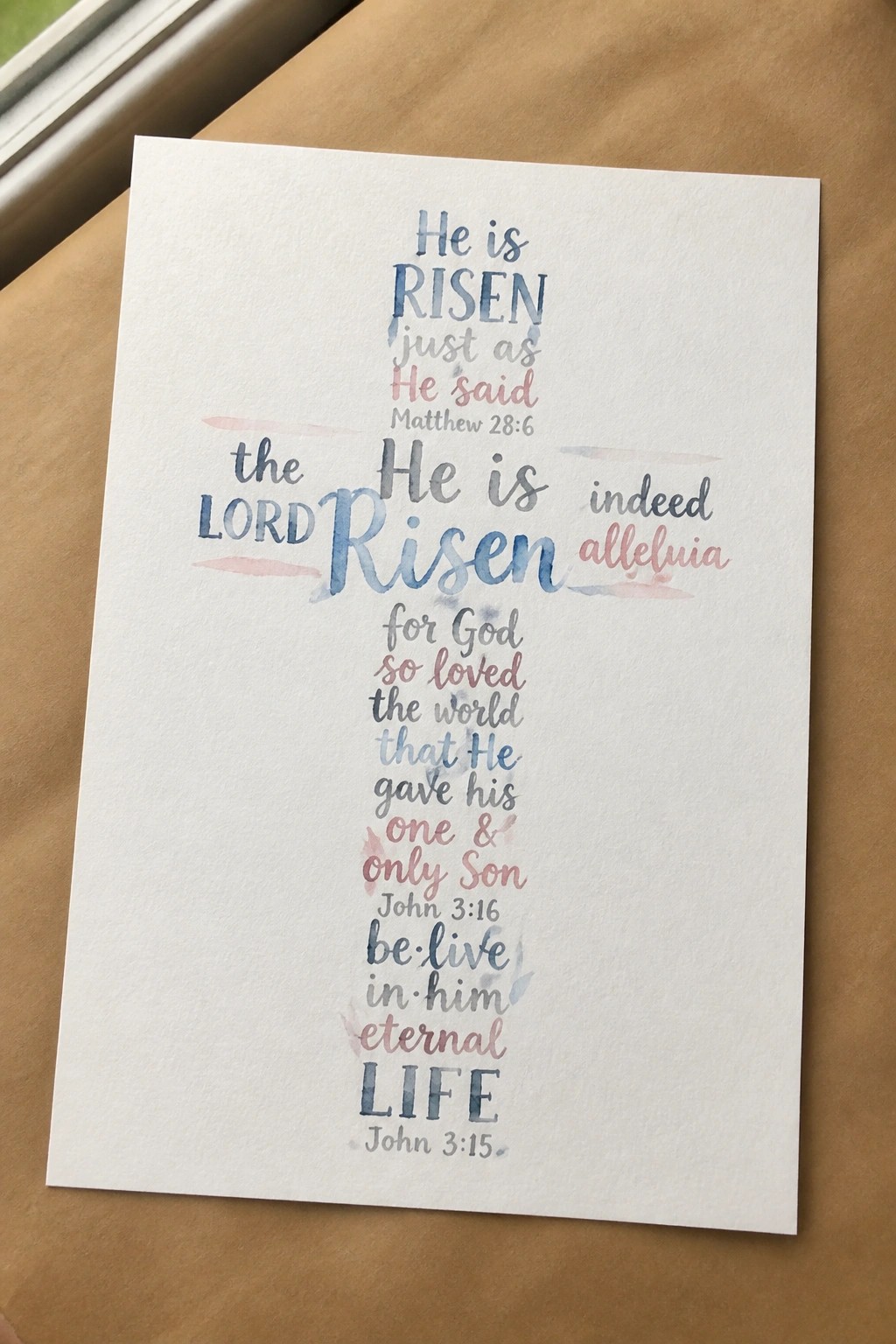 Watercolor cross of Bible verses in blue and pink on white paper.