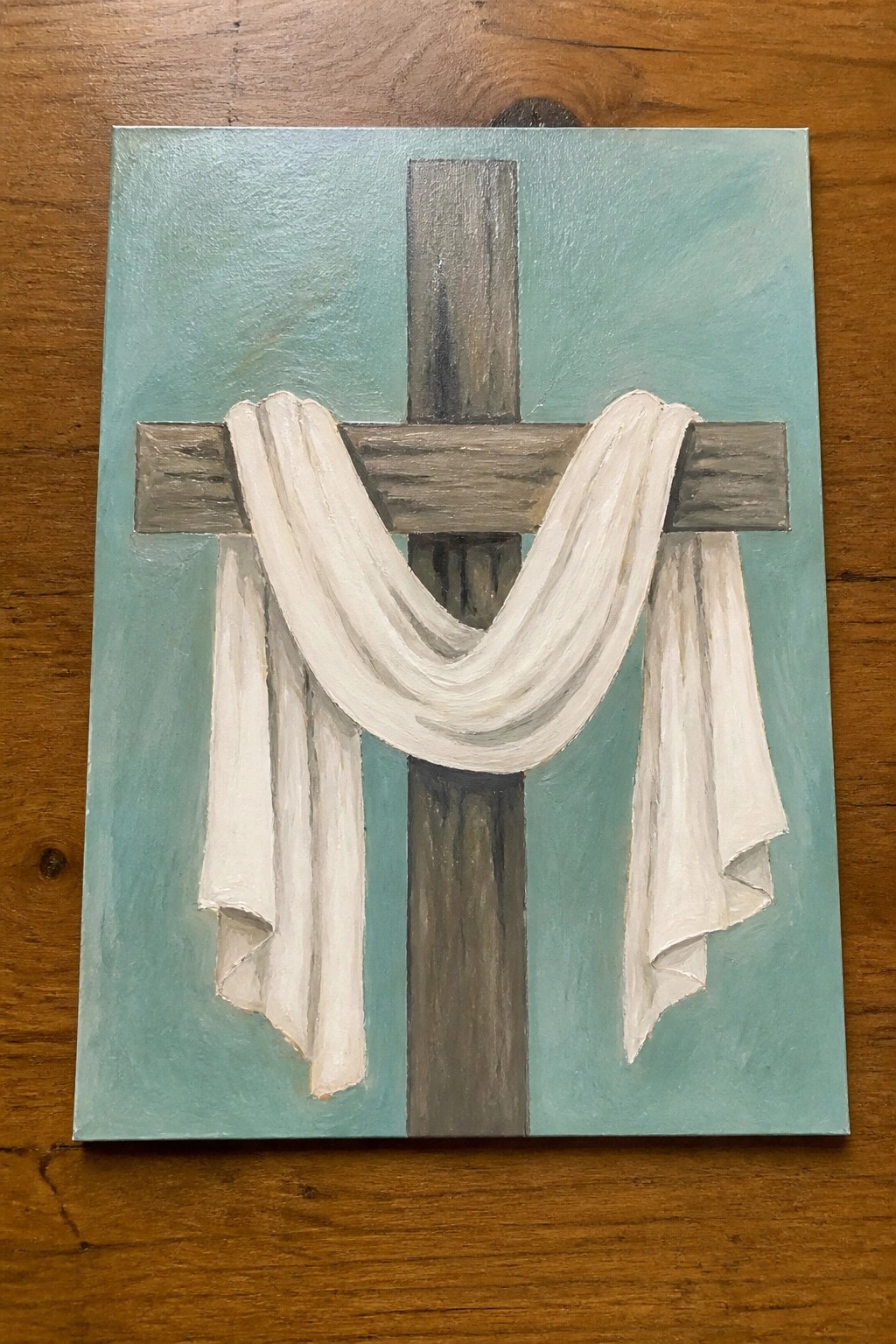 Wooden cross draped with flowing white cloth on teal painted background