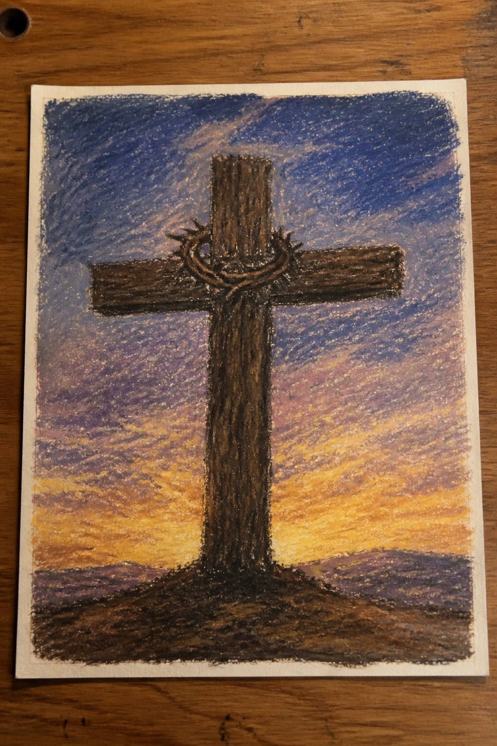 Wooden cross with crown of thorns on hill under blue-purple-orange sunset sky