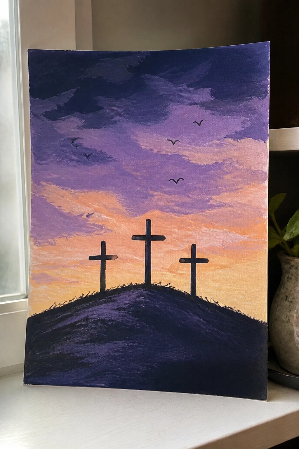 Three crosses on a hill under purple-orange sunset sky with flying birds.