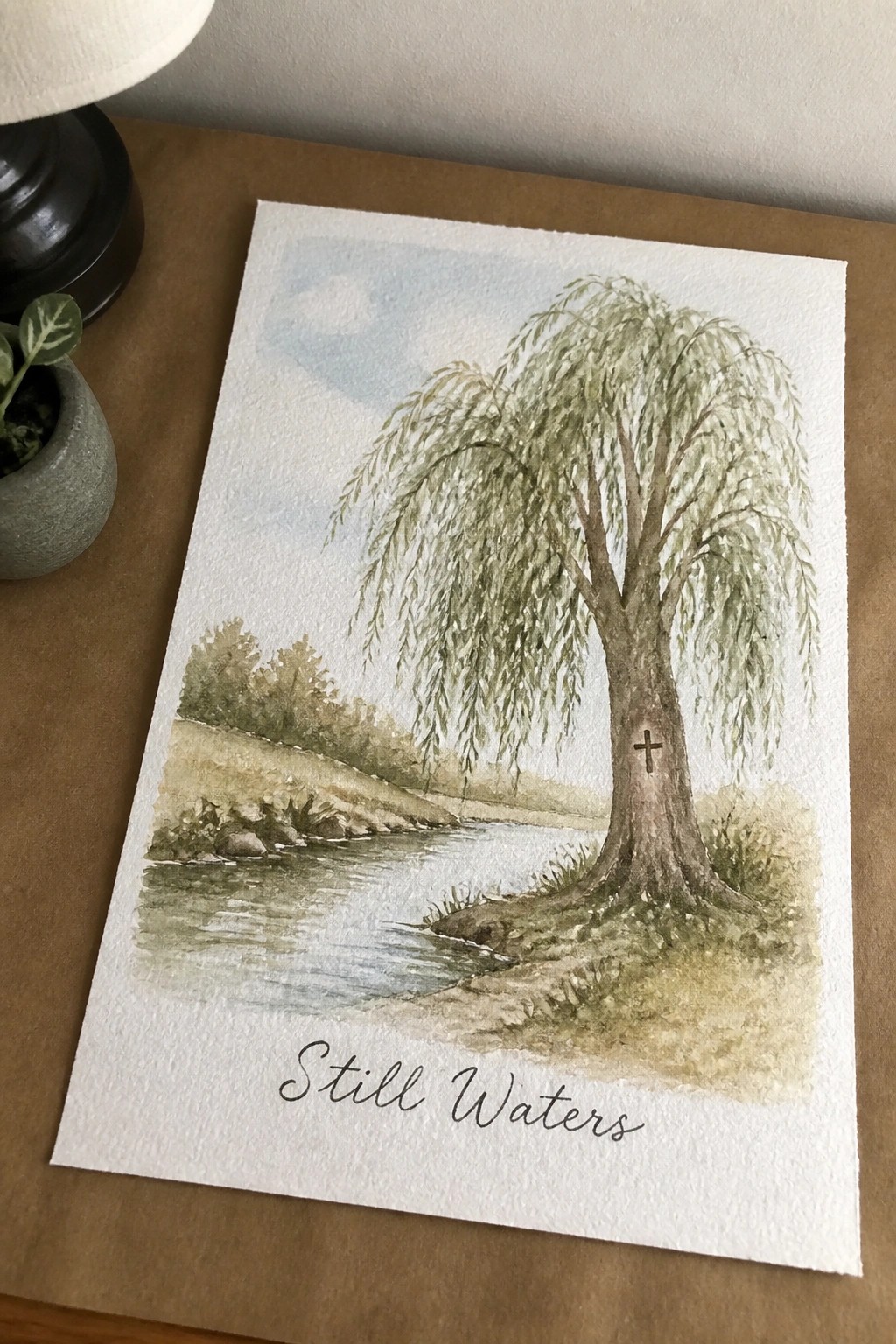 Watercolor of weeping willow with cross by river, titled Still Waters