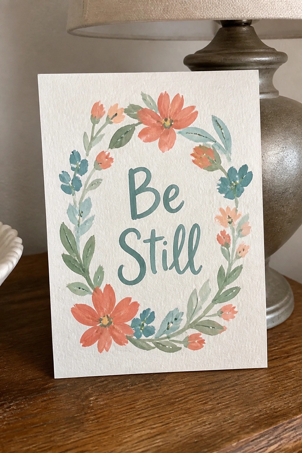 A white card with a watercolor floral wreath in coral and teal tones surrounding the words 