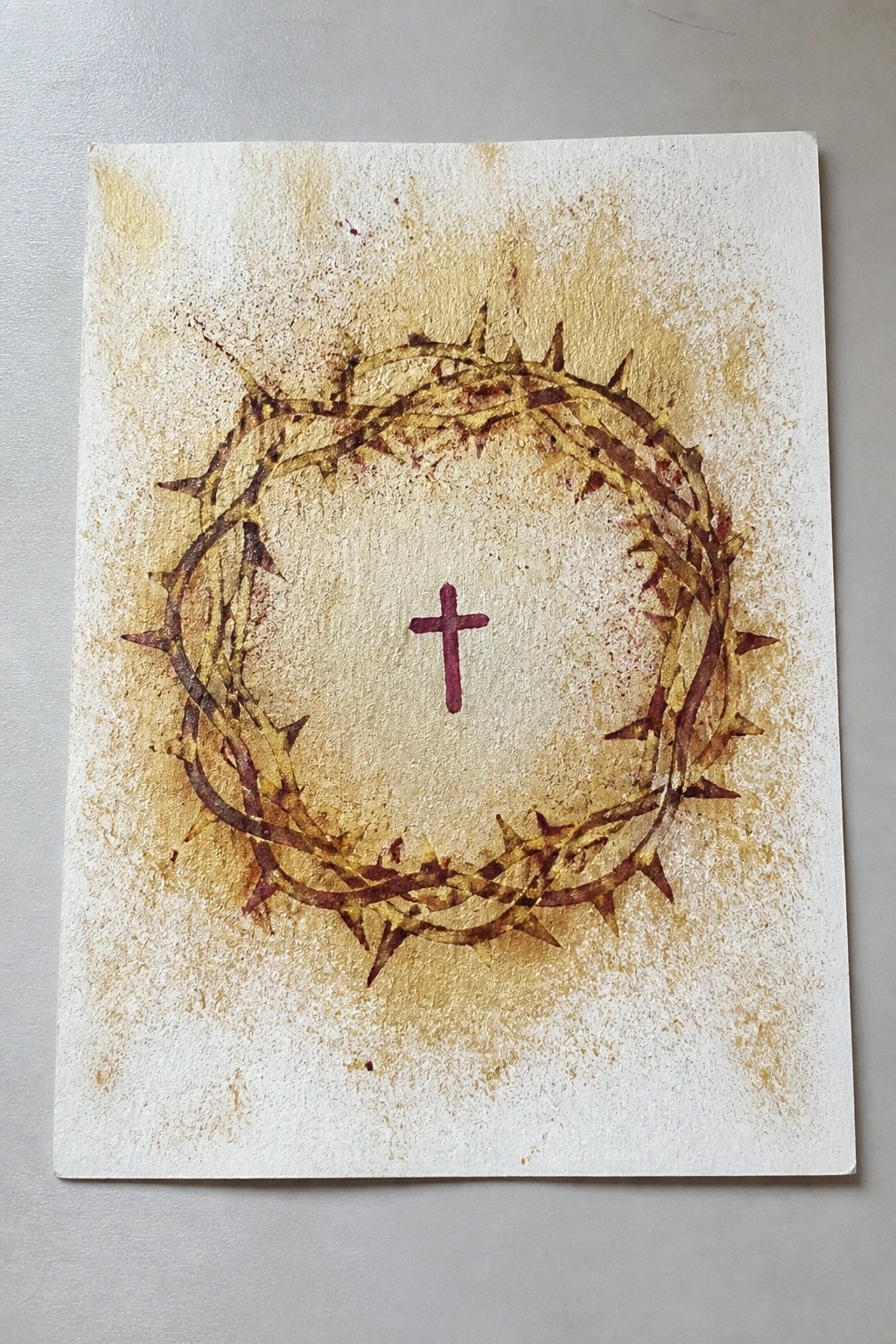 Watercolor painting of thorny crown encircling small purple cross on stained paper.
