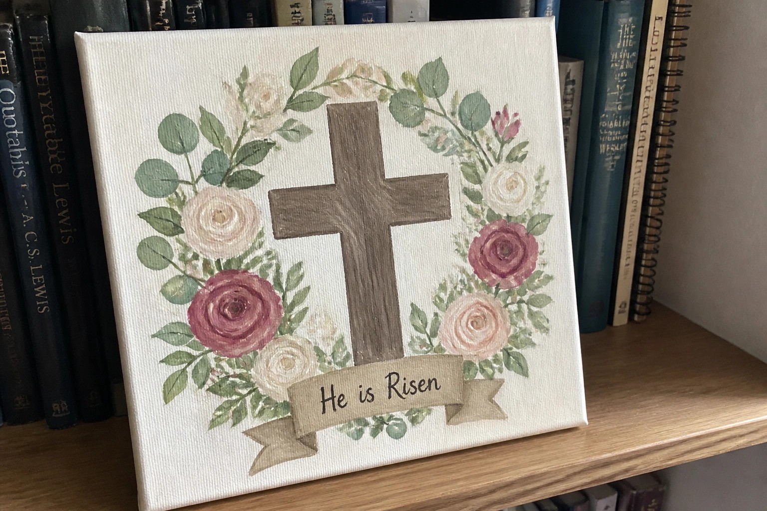 Brown cross in pink rose wreath with "He is Risen" banner on canvas
