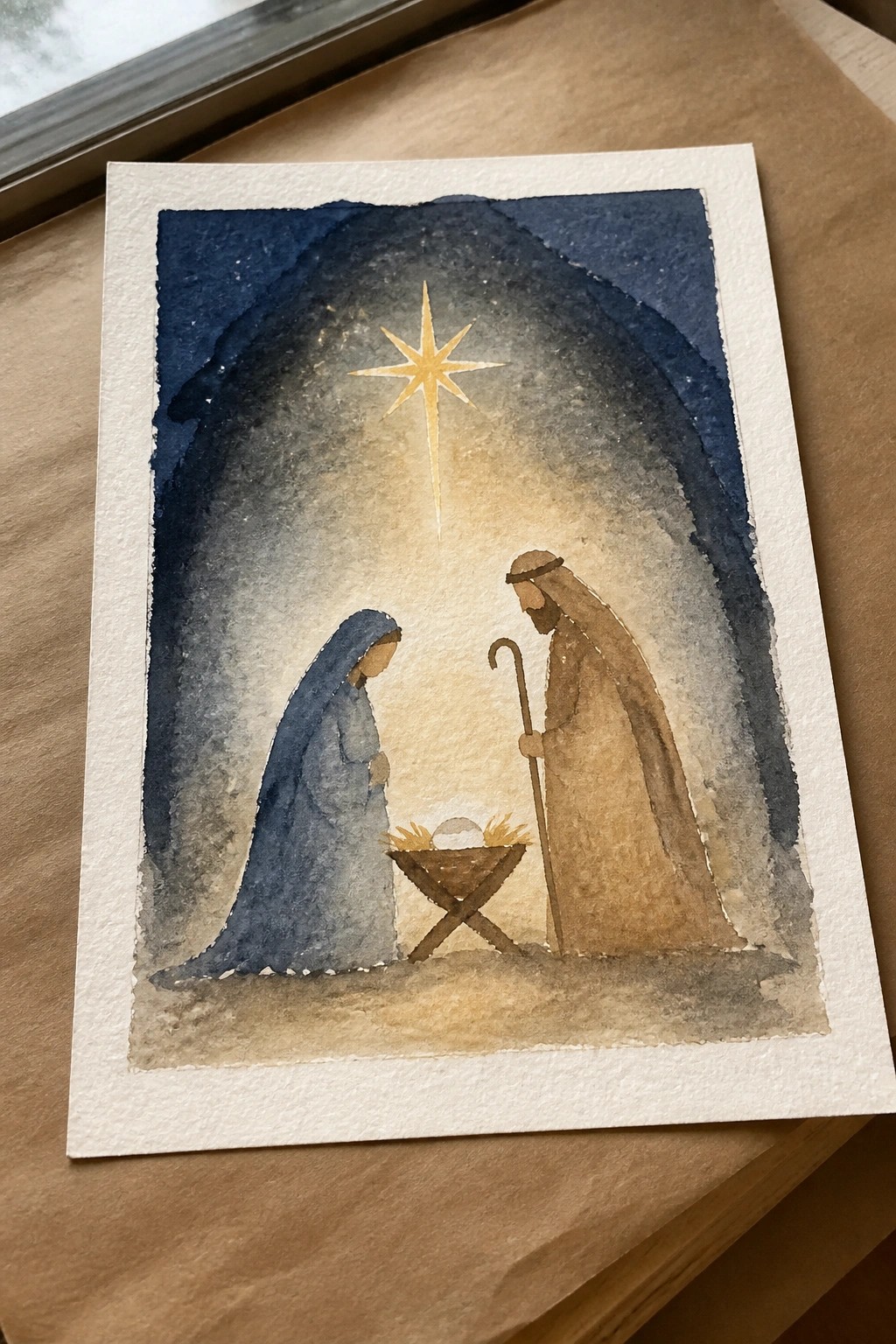 Watercolor nativity with Mary in blue robe, Joseph with staff, and bright star over manger