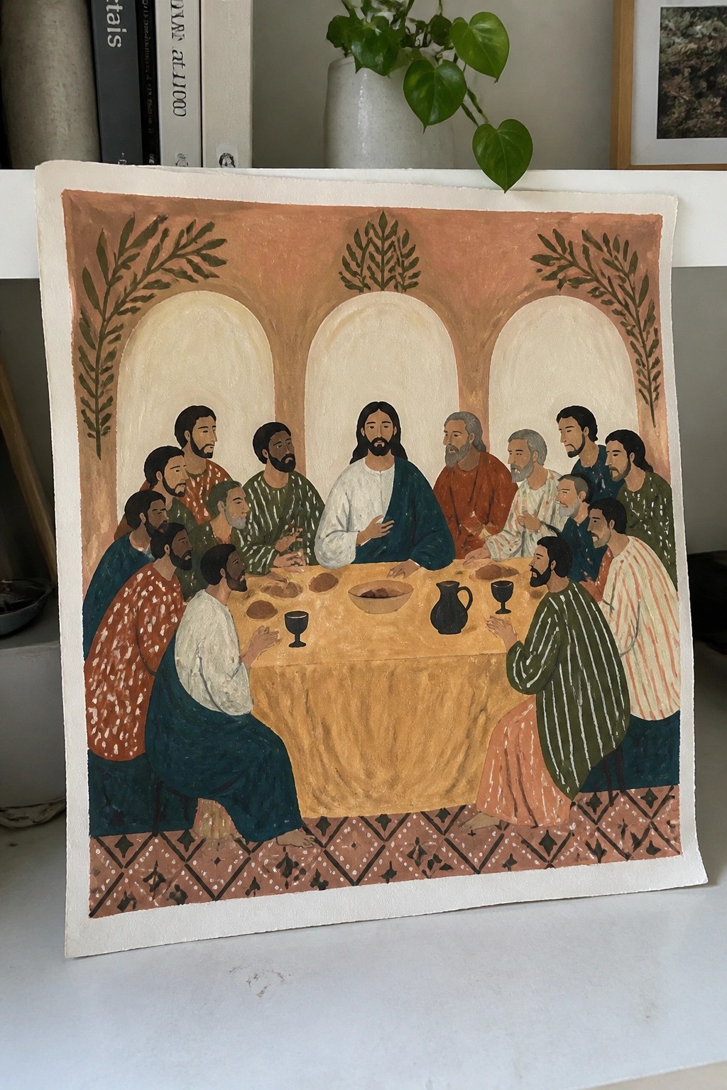 Stylized painting of Jesus and apostles seated at a table with bread and goblets.