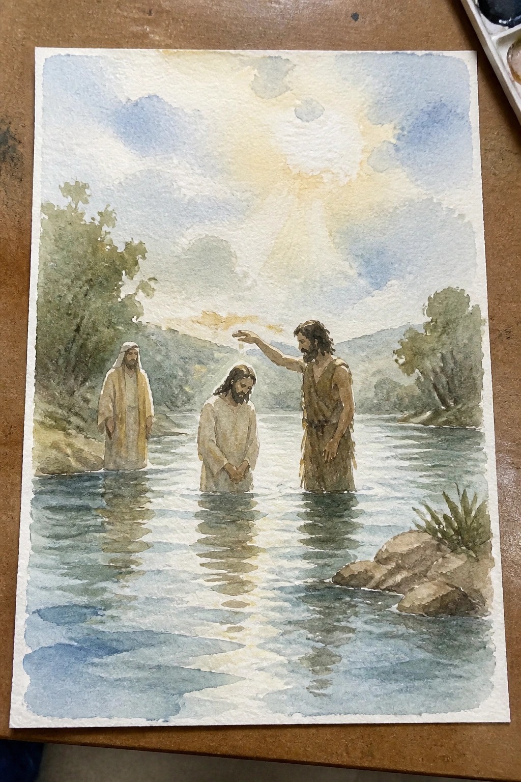 Watercolor of three robed men in a river, one baptizing under glowing sky.
