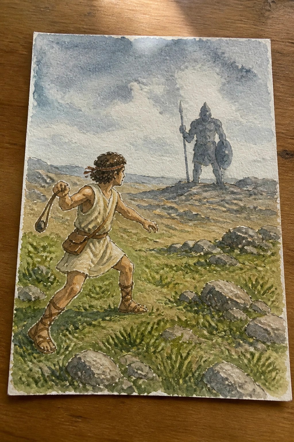 Watercolor painting of boy with sling facing armored warrior on rocky hill