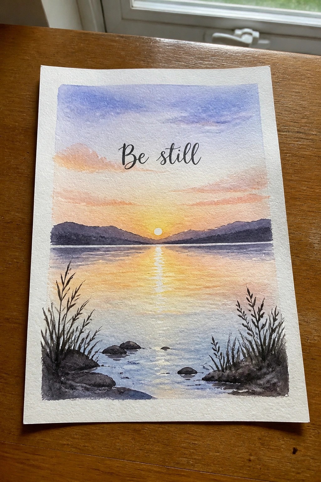Watercolor sunset over lake with mountains, sun reflection, reeds, and 