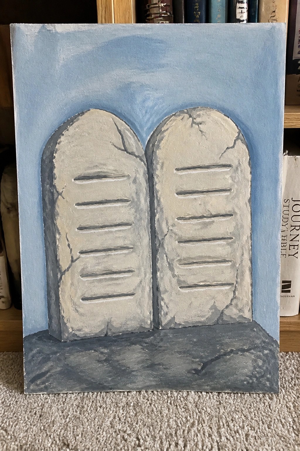 Two cracked stone tablets with lines on blue sky and rocky base painting