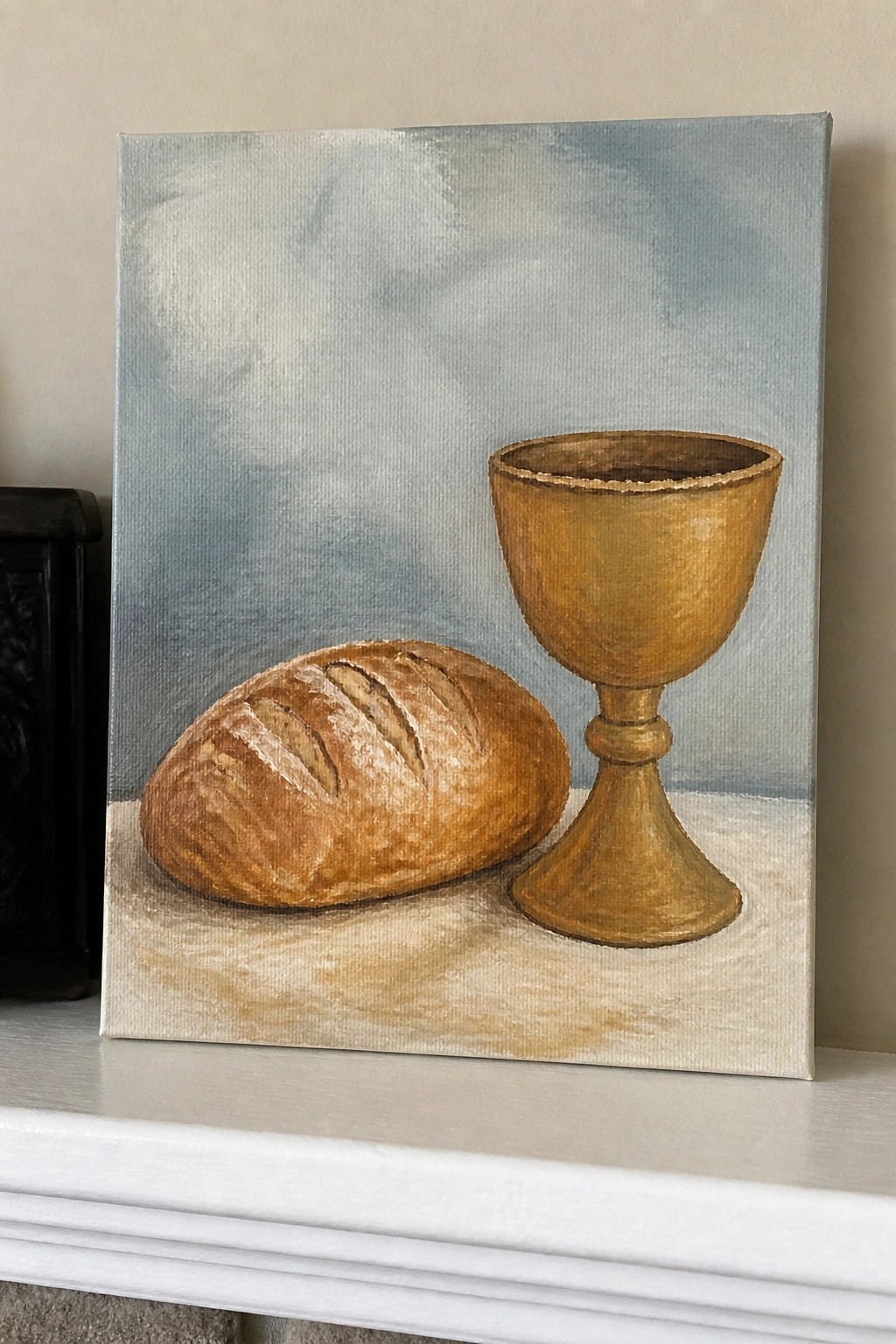 Still life painting of crusty bread loaf beside golden chalice on white surface
