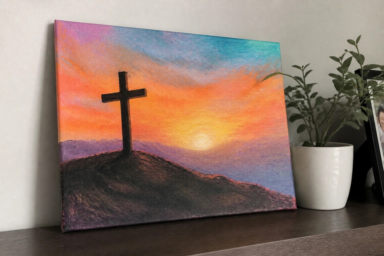Silhouetted cross atop a hill against a vibrant orange-pink sunset sky.