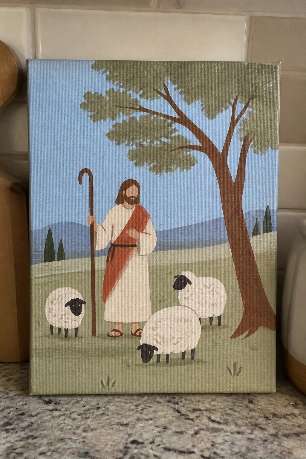 Jesus in white robe with red sash holds crook near three sheep under tree in field
