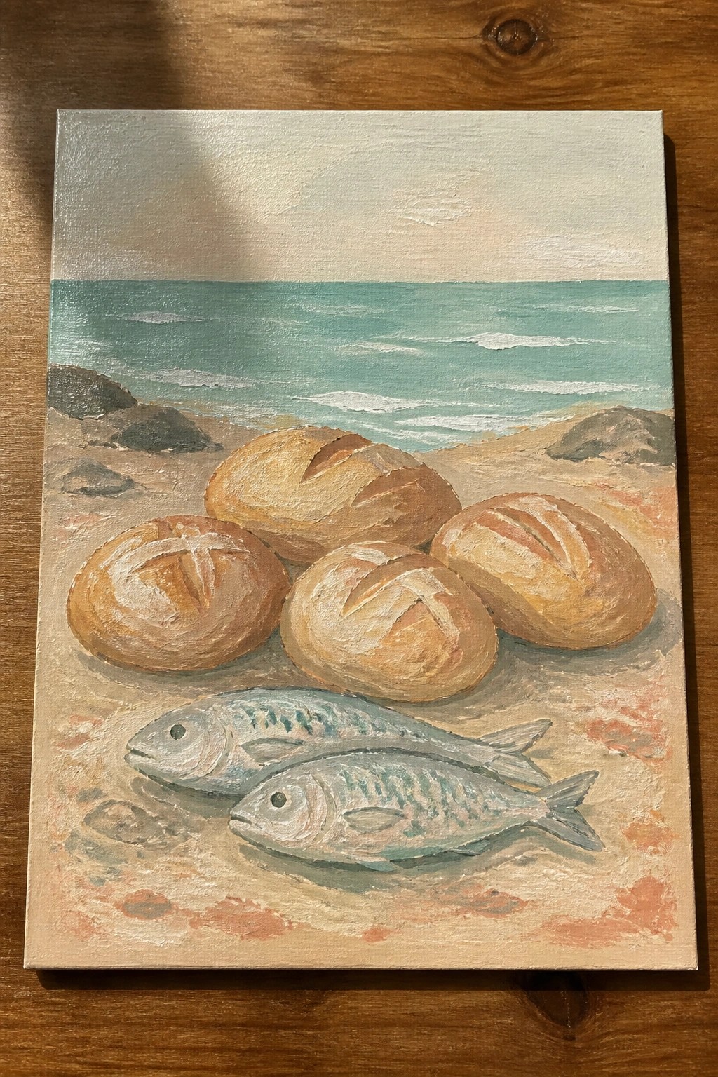 Painting of bread loaves and fish on sandy beach with turquoise ocean waves