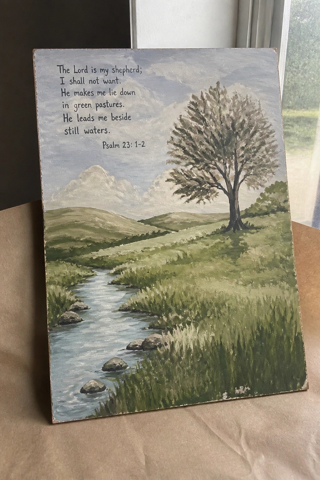 Pastoral landscape painting with winding stream, green hills, lone tree, and Psalm 23 text.