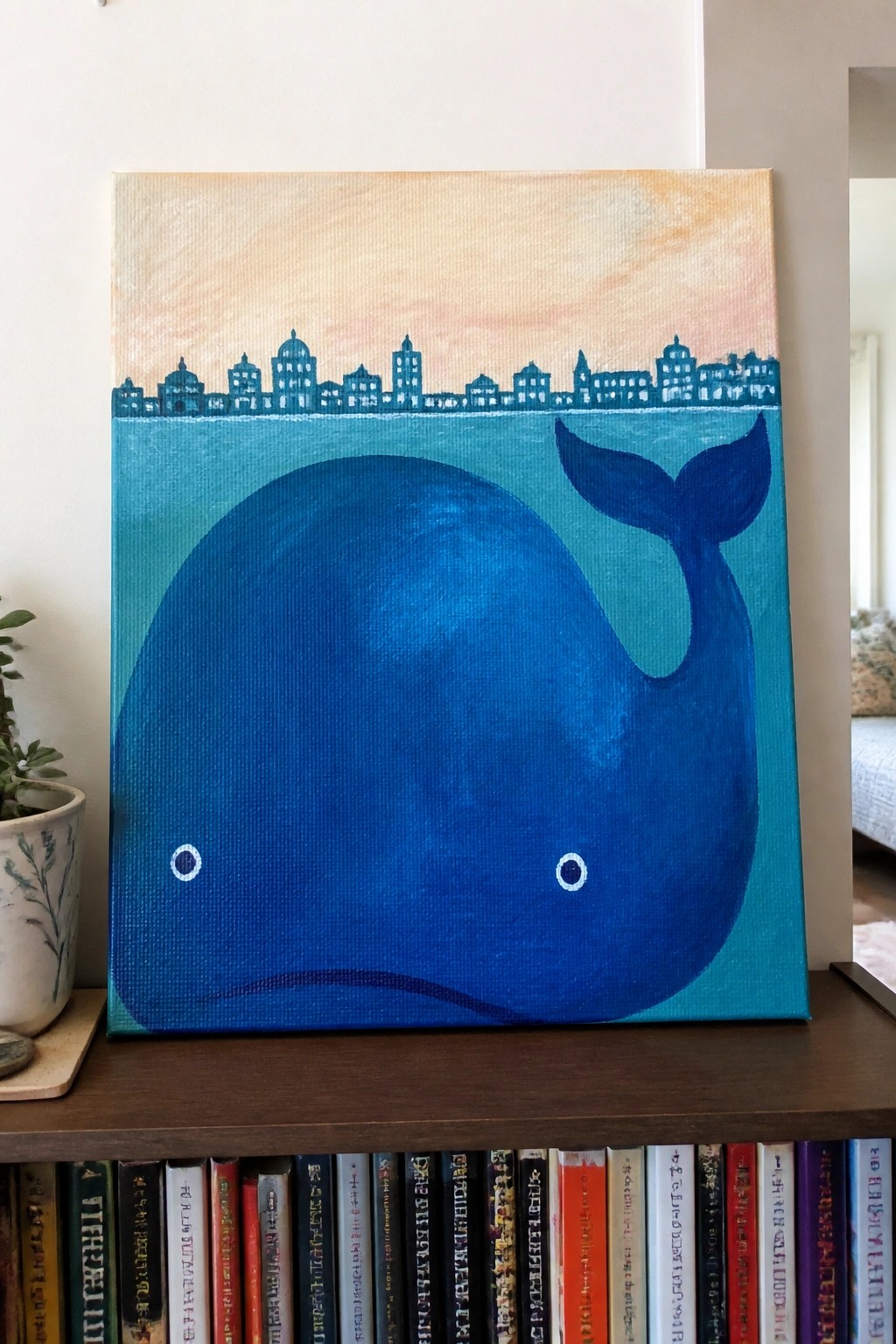 Blue whale painting with city skyline above row of books on shelf