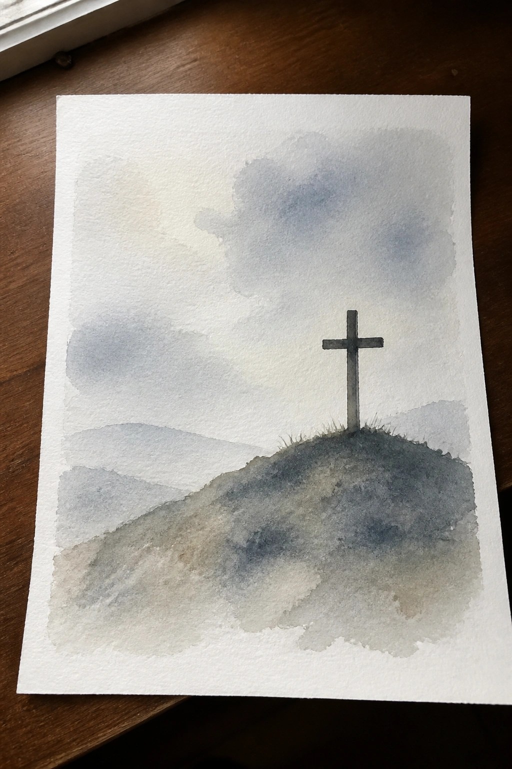 Watercolor of a cross on a dark hill under cloudy skies with distant mountains