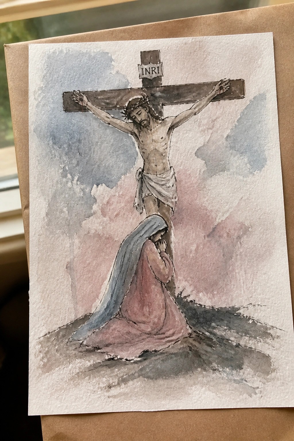 Watercolor of Jesus crucified on cross with INRI sign, Mary kneeling in prayer below.