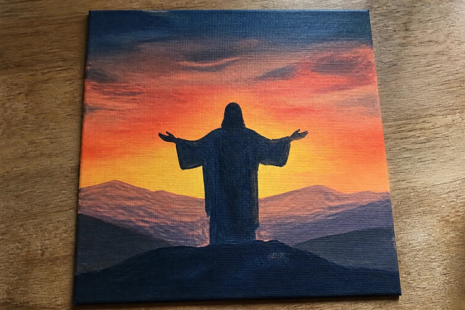 Silhouetted robed figure with arms outstretched atop hill under vibrant sunset sky.