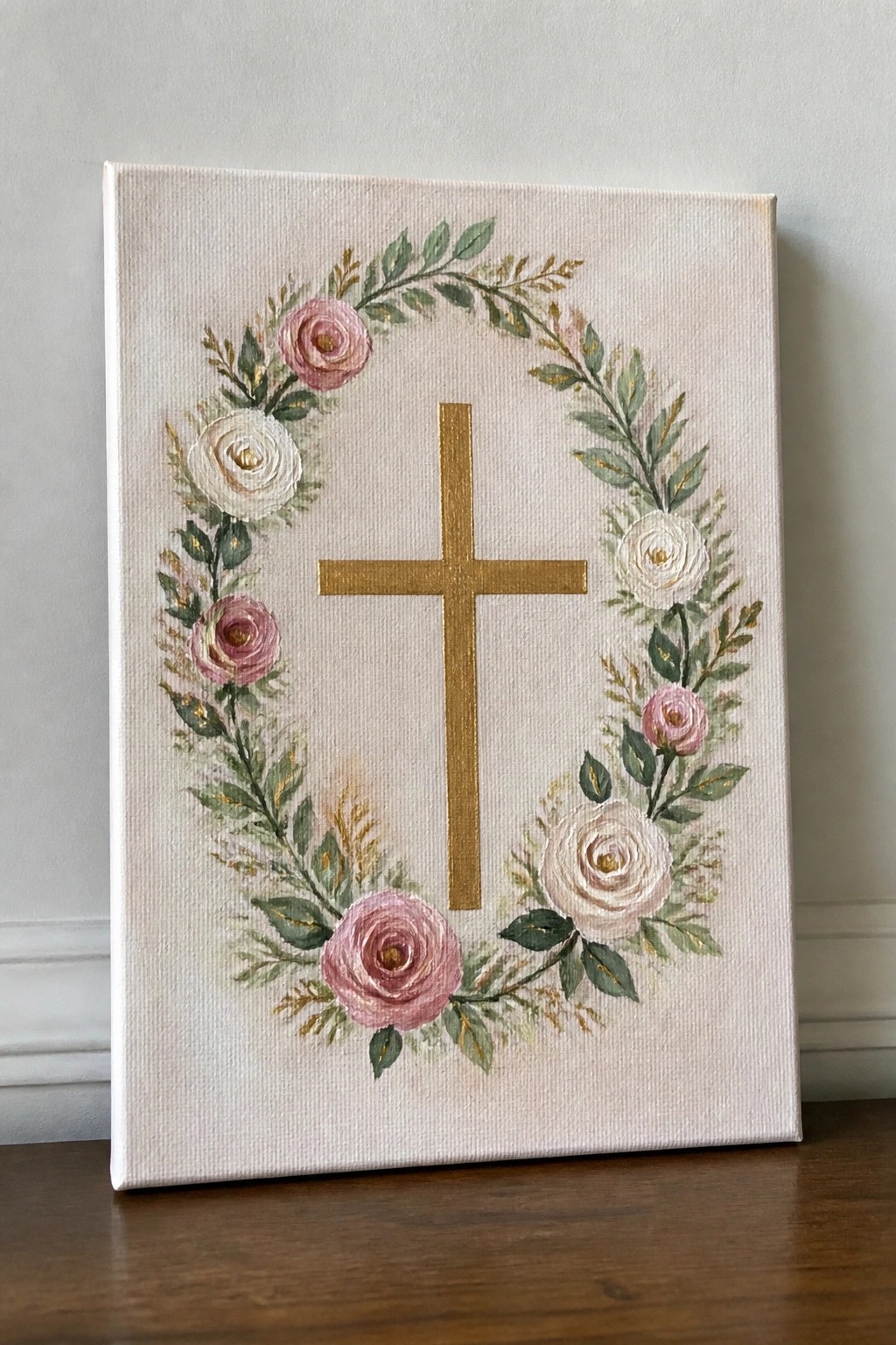 Golden cross centered in floral wreath of pink white roses and green leaves on canvas.