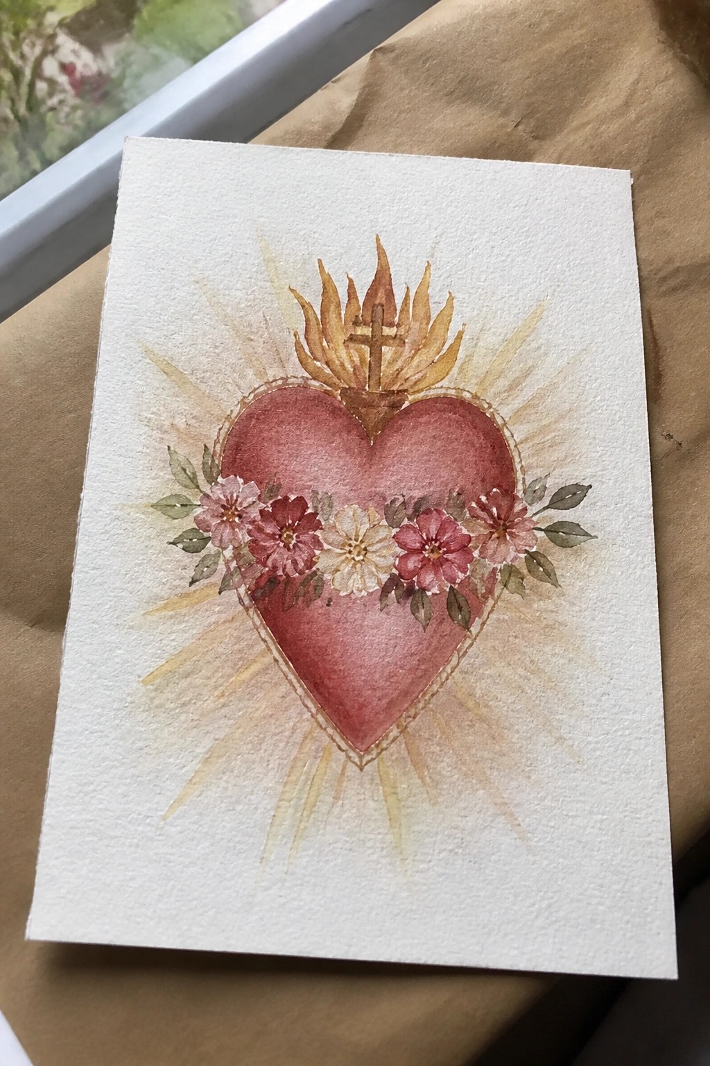 Watercolor red flaming heart with cross, pink flowers, and golden rays on white paper.